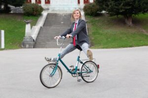 Marie Burneleit auf einem Fahrrad vor der Bavaria. Sie streckt die Beine von den Pedalen und lächelt